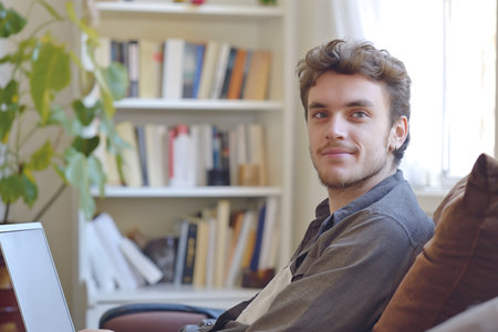 young man sits in light beautiful room with laptop and booksの素材