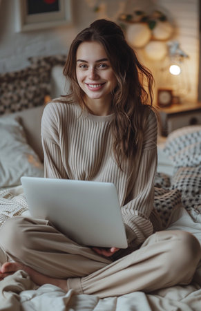 A joyful woman sits on her bed, using a laptop with contentment and relaxationの素材