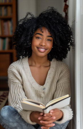 Beautiful black woman sitting on the floor of her hallway holding an open notebook and pencilの素材