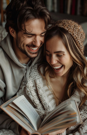 A joyful couple relaxes on the sofa at home, reading a book and laughing togetherの素材