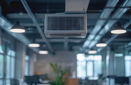 An air conditioner unit mounted on the ceiling in an office workspace providing coolingの素材