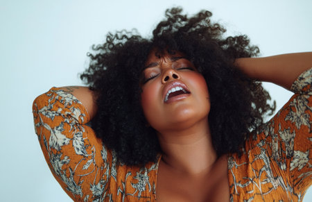 A plus-size Black woman with afro hair screams in pain, holding her head in distressの素材