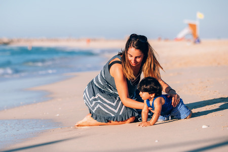 portrait of a beautiful baby boy playing on the shoreline with his motherの写真素材