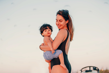 portrait of a beautiful baby boy playing on the shoreline with his motherの写真素材