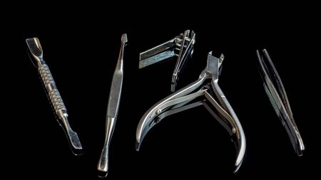 Manicure and pedicure accessories on a black glass table. Equipment and tools for nail treatment. Hand care. Scissors,pliers,tweezers and blade on the table.の写真素材