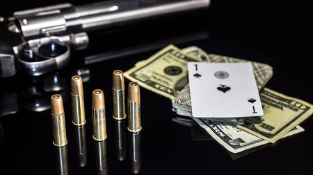 Dangerous gambling for money. A pistol with cartridges, money dollars and a deck of playing cards with an ACE of spades lie on a glass table. Dangerous gambling debts and loans.の写真素材
