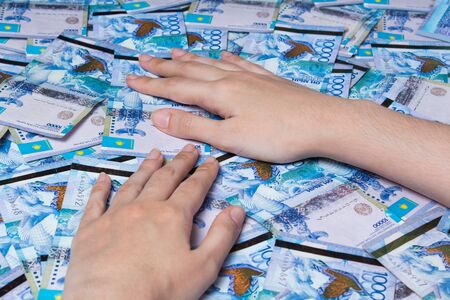 Hands are on a table full of Kazakhstan tenge money. Paper banknotes tenge KZT. Tenge is the...