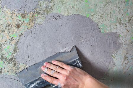 Plaster the wall with a putty knife.Internal construction and finishing works.The Builder puts plaster on the wall.Hand holding a spatula with construction mix and smoothes out bumps.Repair the wallの写真素材