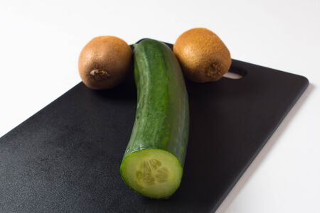 A cucumber and two kiwis lie on a black cutting Board. Diet food and salads for a healthy lifestyle. The likeness of a phallic symbol or masculine dignity. Fresh vegetables and fruits.の写真素材