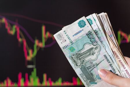 Hands holding Russian rubles in front of a computer monitor with the currency market and Forex...