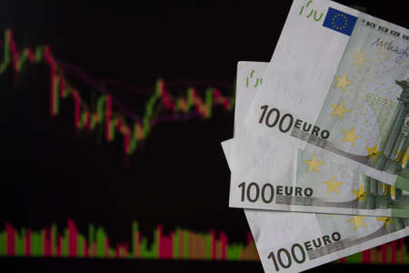 Hands holding euro, EUR in front of a laptop monitor with a price chart.Forex and trading.A trader trades stocks,bonds and securities or currencies on the Forex market or stock exchange for euroのeditorial素材