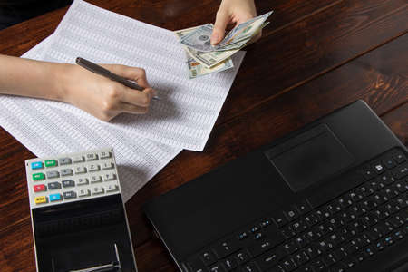Obligation to pay wages and debts in the company.A cashier holds money dollars over an office work space with documents, a cash register, a phone, and a computer.Work in the office with financesのeditorial素材
