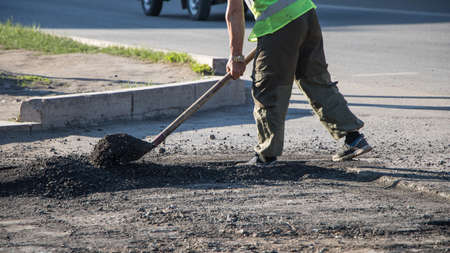 Workers repair the road surface and asphalt the street. People in overalls with shovels throw dirt and fill up holes in the road. Road works.のeditorial素材