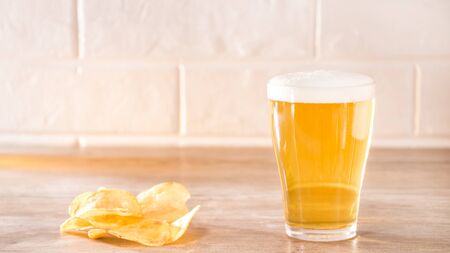 Fresh foamy beer with chips lying on a wooden table in the morning sun.の写真素材
