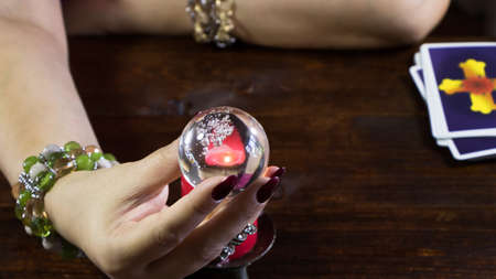 New York, USA-19.05.2020: A fortune teller holds a magic ball.On the table are fortune-telling cards and lighted candle.Magic sessions with clairvoyance cards.Reading maps by candlelightのeditorial素材