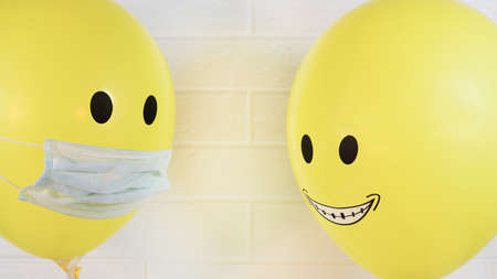 Two smiling yellow balls, one in a medical mask is quarantined for an epidemic of a virus, flu, Allergy or covid 19.の写真素材