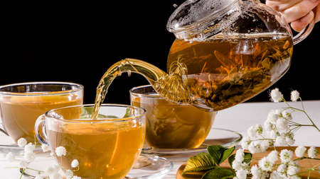 Pour the brewed green tea from the teapot into a mug.Tea parties, tea ceremonies, and Zen-style traditions. A Cup of green tea and a teapot.Flower tea with fruit slices.Tea ceremony, traditional drinkの写真素材