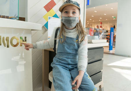 A baby girl wearing a protective medical mask at a shopping Mall during a coronavirus quarantine.の写真素材