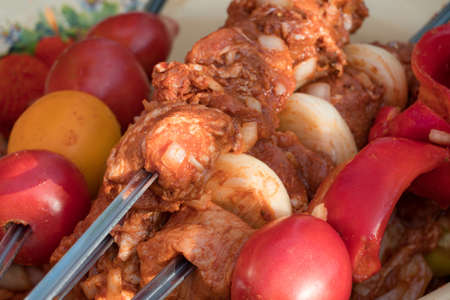 Marinated raw meat for shish kebab, barbecue or grill with onions, tomatoes and bell peppers on skewers. Cooking meat in the grill on skewers in nature in the summer on a picnic.の写真素材