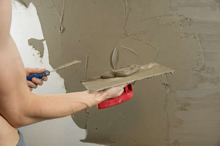 A worker plasters the wall with a spatula and applies a cement mix solution. The repairman lays the...