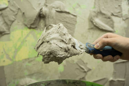 A worker uses a spatula to get a solution of the cement mixture. The master puts the plaster....