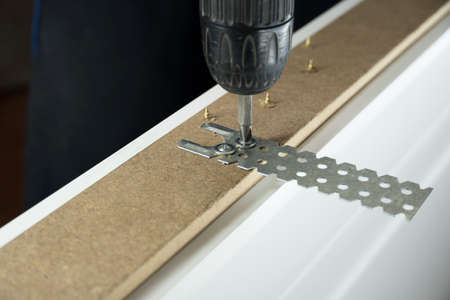 A worker twists a screw into the Board with a drill. The handyman does housework and improves the...