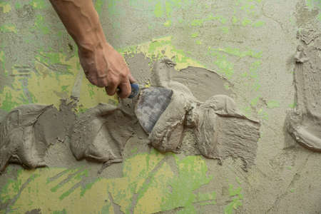 A worker plasters the wall with a spatula and applies a cement mix solution. The repairman lays the...