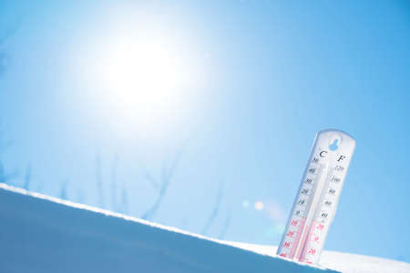 The thermometer lies on the snow and shows a negative temperature in cold weather on the blue...