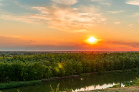 The heavenly light of the sun over the river and the forest.Dramatic evening sky with clouds and rays of the sun.Golden hour at evening sunset or morning sunrise.Panoramic view of cirrus cloudsの写真素材