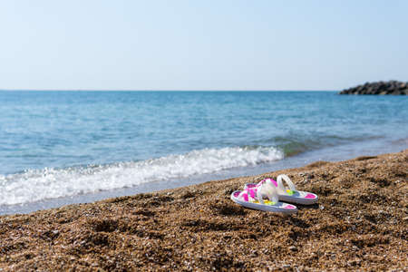 Colorful flip flops on the sunny sandy beach with turquoise water. Island vacation on hot summer day. Beautiful sea waves in the background. Summer seascape. Recreation.の写真素材