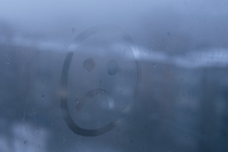 Very sad emoji on the foggy glass. Unhappy face sign close-up on the window. Selective focus on photo. Concept of depression and sadness.の写真素材