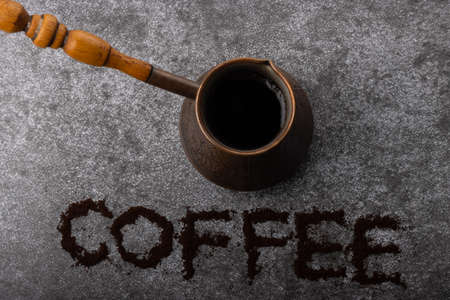 Top view of vintage cezve with brewed coffee and lettering "coffee" with ground coffee under the cezve on gray background.の写真素材