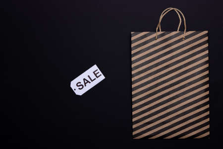 Black Friday concept. Top view of paper craft bag with black stripes and sale tag on black background. Copy spaceの写真素材