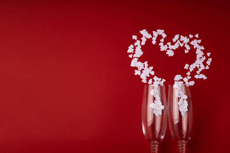 Two glasses with white hearts and splashing in heart shape on red background. Valentine's Day, February 14, love concept. Flat lay, top view, copy space.の写真素材