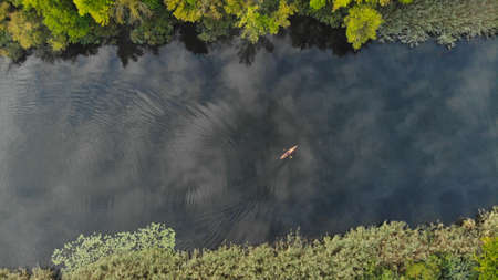Top aerial view of the river along which a small orange kayak floats. Green trees grow on the shore. Ukraine, Europeの写真素材