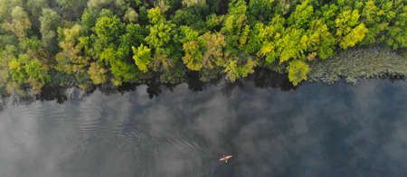 Top aerial view of the river along which a small orange kayak floats. Green trees grow on the shore. Banner. Ukraine, Europeの写真素材