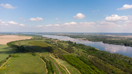 Aerial view of green fields and forest with trees and a river across which the railway bridge....