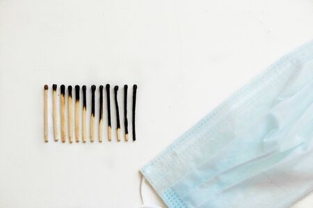 Burned matches in a row on a white background and medical mask