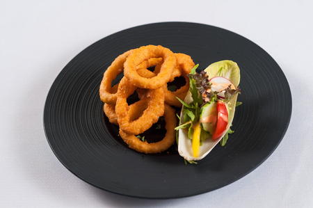 Fried onion rings with vegetables salad on a black plateの写真素材