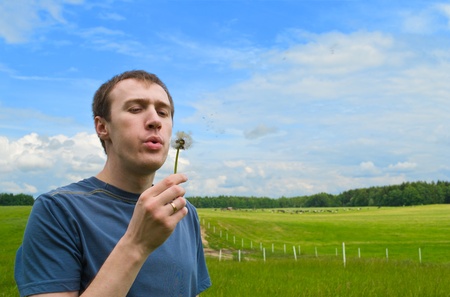 The young man blows on a dandelion on a green meadowの写真素材