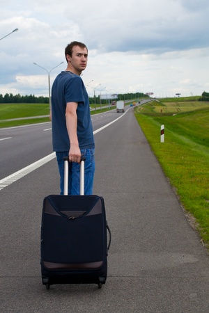 The young man pending on road with a suitcaseの写真素材