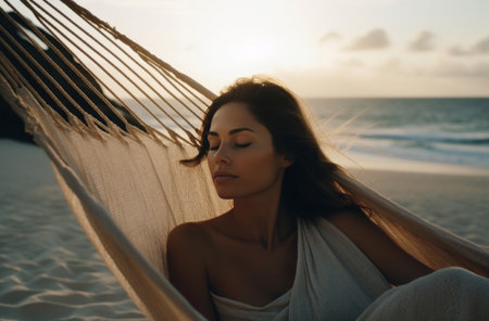 woman sitting in hammock on the beach with her eyes closedの素材