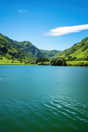 A serene lake surrounded by lush green mountains and a clear blue sky in the background.の素材