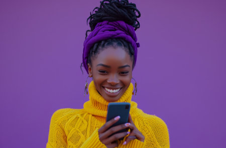 black woman using cell phone and smiling in background against purple.の素材