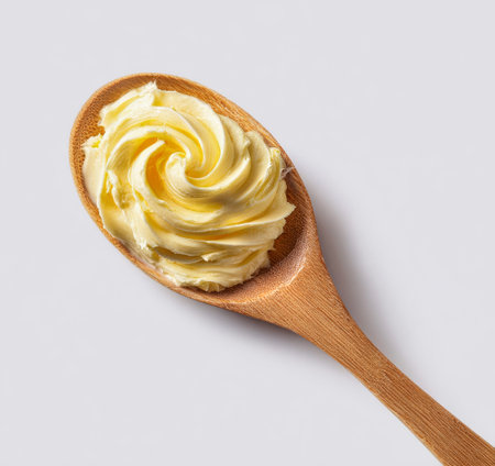A wooden spoon holds a swirl of creamy butter, showing a smooth texture and rich color against a neutral background. Ideal for cooking or baking inspiration..の素材