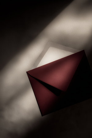 A red envelope rests on a surface, partially illuminated by soft light, showing a silver lining inside. This scene suggests anticipation or the promise of a special message.の素材