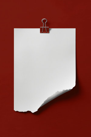 A piece of blank torn paper is hanging on a red wall using a metal clip. The edge is slightly curled, giving it an informal look suitable for notes or reminders.の素材