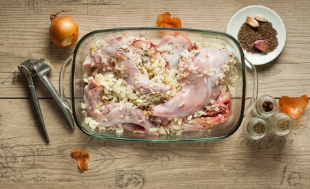 raw rabbit meat in roaster with onion cumin and garlic on wooden vintage tableの写真素材