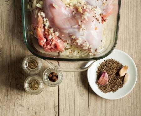 raw rabbit meat in roaster with onion cumin and garlic on wooden vintage tableの写真素材