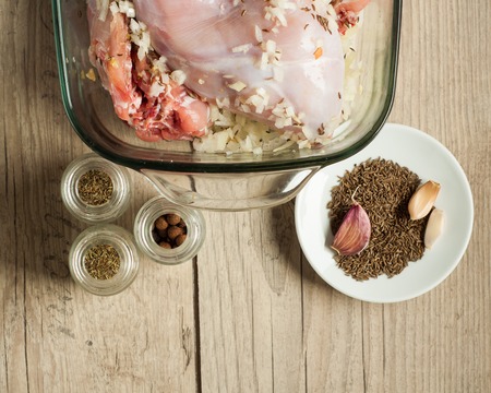 raw rabbit meat in roaster with onion cumin and garlic on wooden vintage tableの写真素材